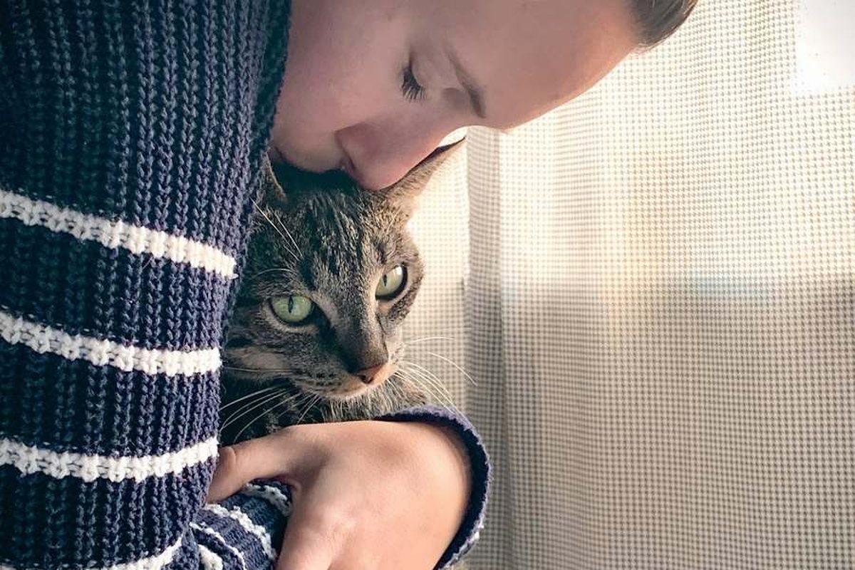 A young woman holds a tabby cat and presses her face into its fur